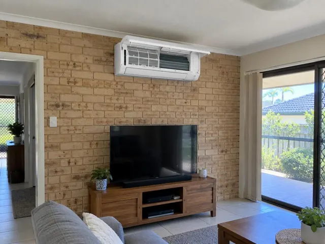 Clean split system with open front panel on a brick feature wall in a modern living room in Labrador