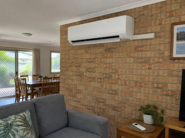 Living room with a wall-mounted split system on a brick feature wall in a home in Parkwood