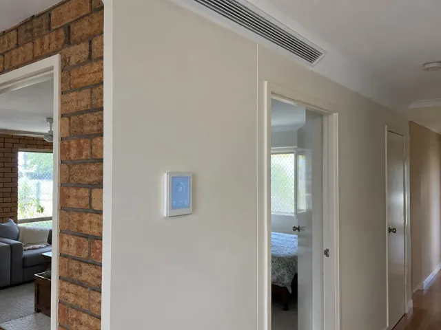 Ceiling duct outlet and wall controller in a beige hallway with brick interior wall in Coombabah