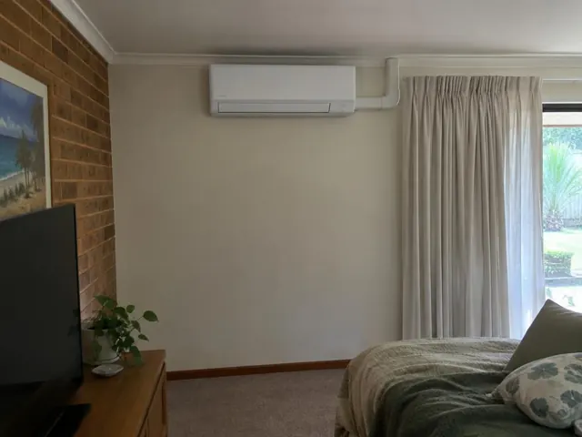 Wall-mounted split system above curtains in a carpeted living room with brick feature wall in Arundel